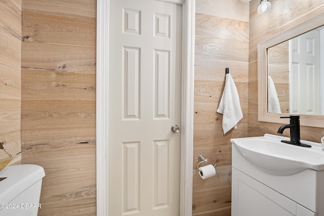 bathroom featuring wooden walls, vanity, and toilet