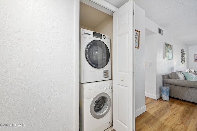 washroom with a textured ceiling, light hardwood / wood-style floors, and stacked washer / drying machine