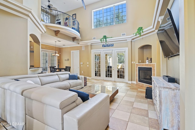 tiled living room with french doors, a notable chandelier, a high ceiling, and a tile fireplace