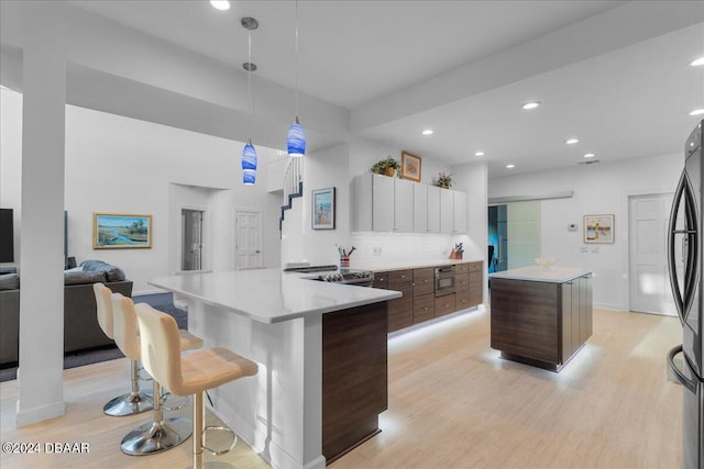 kitchen featuring dark brown cabinetry, a center island, backsplash, decorative light fixtures, and light wood-type flooring