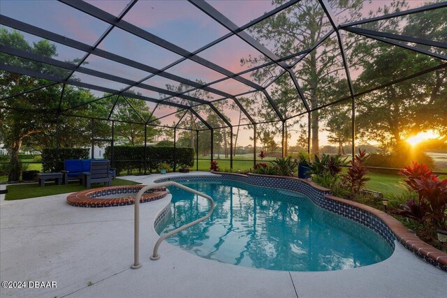 pool at dusk featuring glass enclosure, an in ground hot tub, and a patio