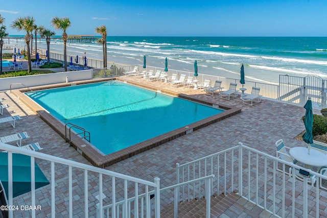 view of swimming pool with a beach view, a water view, and a patio