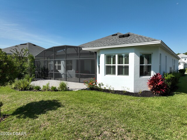 back of property with glass enclosure, a lawn, and a patio