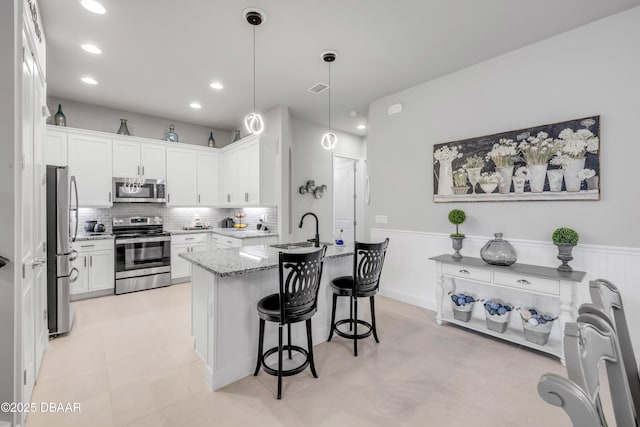 110 Longridge Ln, Ormond Beach, FL 32174 - kitchen featuring appliances with stainless steel finishes, light stone countertops, a kitchen bar, wainscoting, and a sink