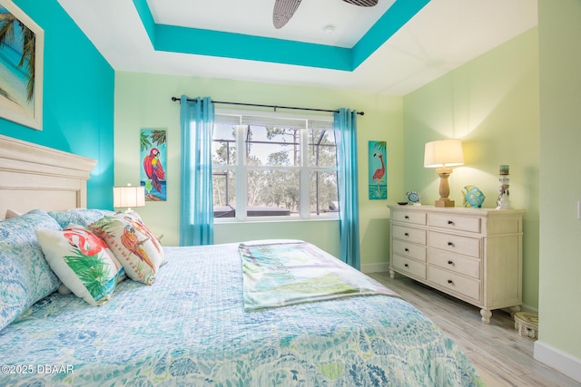 bedroom with ceiling fan, a raised ceiling, and light hardwood / wood-style floors