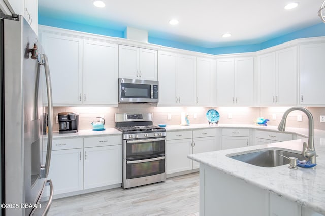 kitchen with sink, stainless steel appliances, white cabinets, and light stone countertops