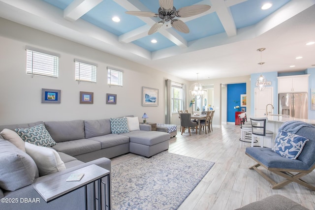 living room with sink, light hardwood / wood-style flooring, beam ceiling, coffered ceiling, and ceiling fan with notable chandelier