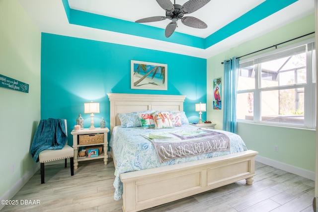 bedroom with ceiling fan, a raised ceiling, and light hardwood / wood-style floors