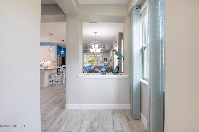 corridor with a healthy amount of sunlight, sink, a notable chandelier, and light hardwood / wood-style flooring