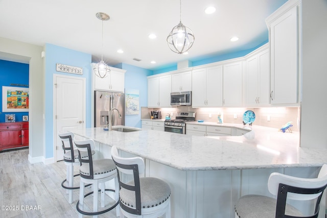 kitchen featuring sink, hanging light fixtures, stainless steel appliances, light hardwood / wood-style floors, and white cabinets