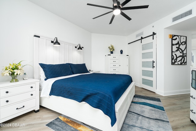 bedroom with a barn door, ceiling fan, and light wood-type flooring