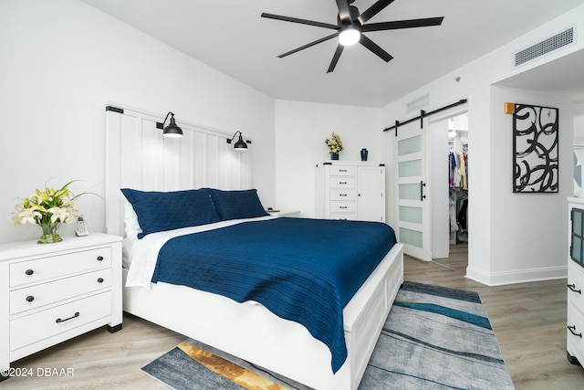 bedroom with a walk in closet, a barn door, ceiling fan, and light hardwood / wood-style flooring