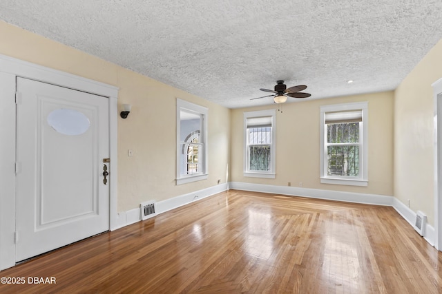 interior space featuring visible vents, ceiling fan, a textured ceiling, light wood-type flooring, and baseboards