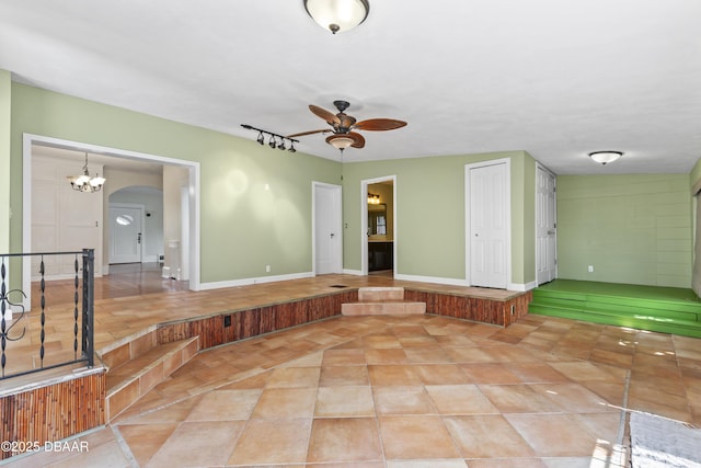 spare room featuring baseboards, ceiling fan with notable chandelier, arched walkways, and light tile patterned flooring