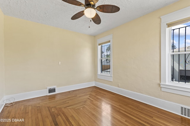 empty room featuring a textured ceiling, wood finished floors, a ceiling fan, visible vents, and baseboards