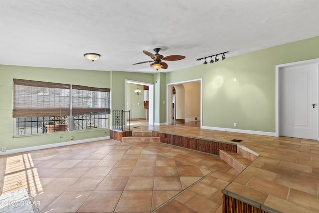 unfurnished room with arched walkways, light tile patterned floors, a ceiling fan, baseboards, and track lighting