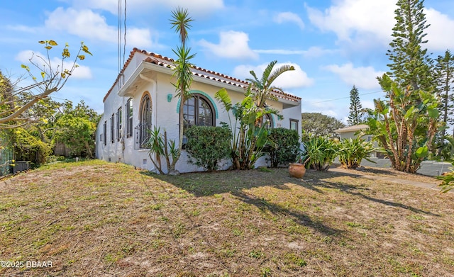 view of side of property with crawl space, a tile roof, a lawn, and stucco siding