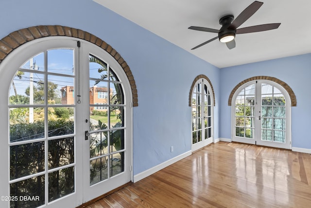 interior space with baseboards, ceiling fan, french doors, and light wood-style floors