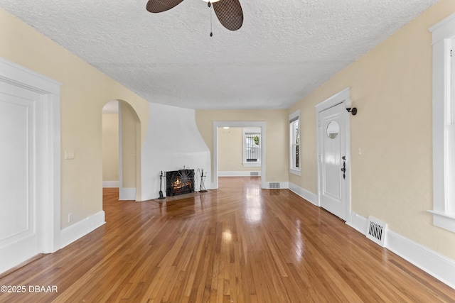 unfurnished living room with arched walkways, visible vents, a large fireplace, wood finished floors, and baseboards
