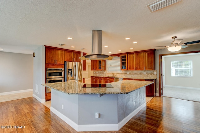 kitchen featuring stainless steel appliances, a spacious island, island range hood, decorative backsplash, and light wood-type flooring