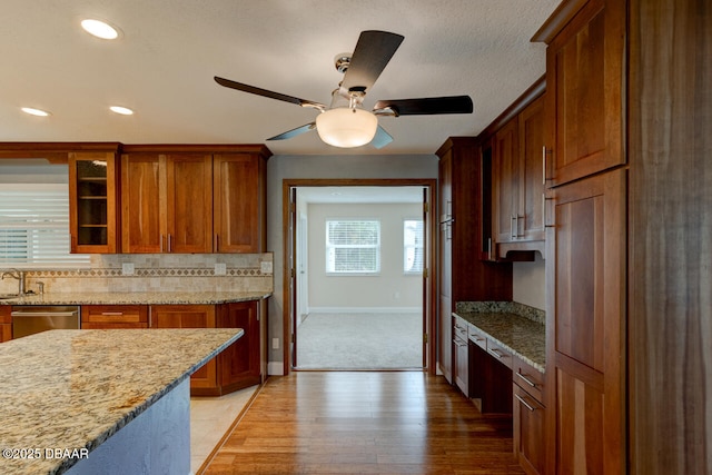 kitchen featuring sink, decorative backsplash, stainless steel dishwasher, light stone countertops, and light hardwood / wood-style flooring