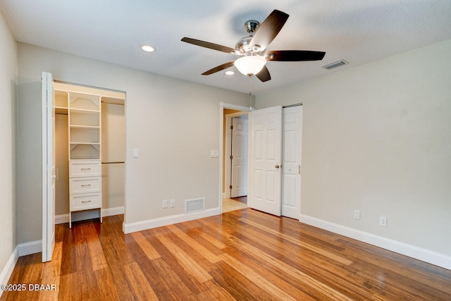 unfurnished bedroom with a walk in closet, ceiling fan, and light hardwood / wood-style flooring