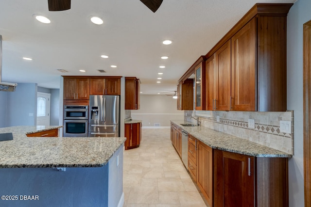 kitchen with appliances with stainless steel finishes, sink, decorative backsplash, ceiling fan, and light stone countertops