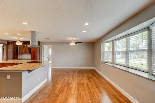 kitchen featuring a kitchen breakfast bar, island exhaust hood, black electric stovetop, light stone counters, and light hardwood / wood-style flooring