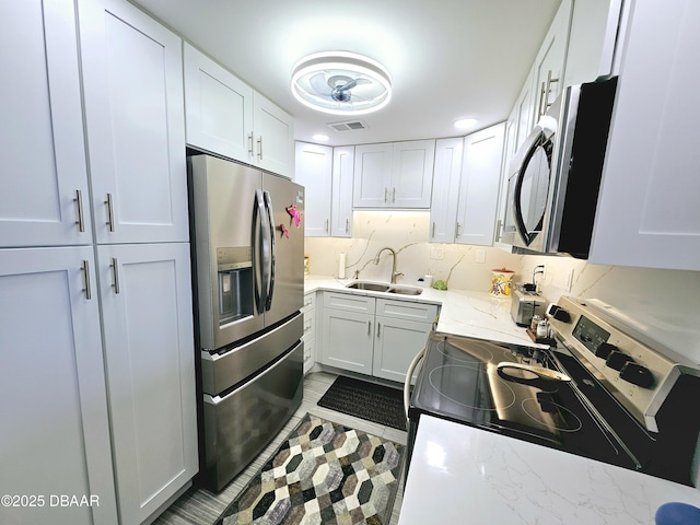 kitchen featuring sink, appliances with stainless steel finishes, tasteful backsplash, light stone countertops, and white cabinets