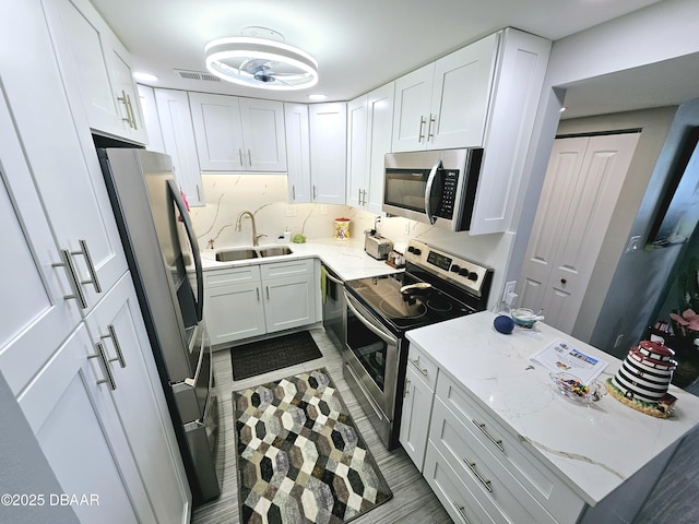 kitchen with sink, appliances with stainless steel finishes, backsplash, light stone countertops, and white cabinets