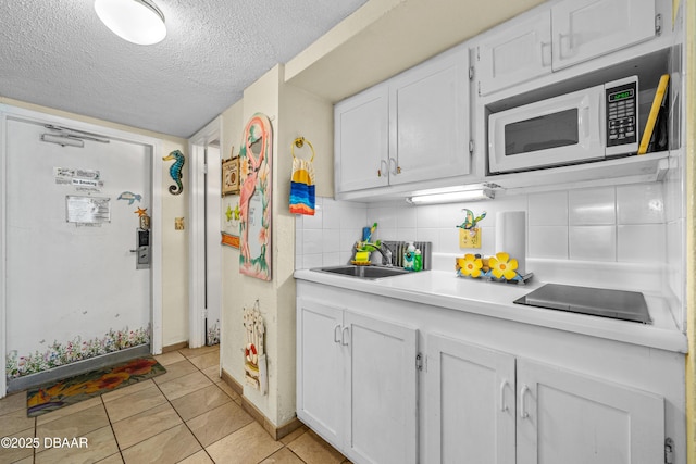 kitchen featuring white microwave, a textured ceiling, light countertops, white cabinets, and a sink