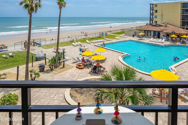 community pool featuring view of water and beach, fence, and a patio area