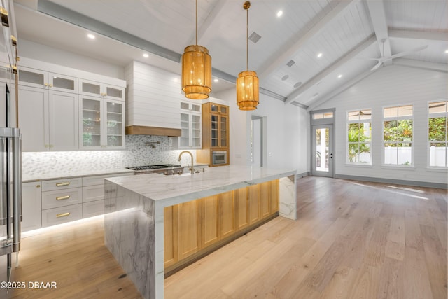 kitchen with vaulted ceiling with beams, a sink, light wood-style flooring, and decorative backsplash