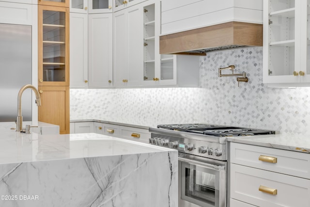 kitchen featuring high end stainless steel range, custom exhaust hood, white cabinetry, and backsplash