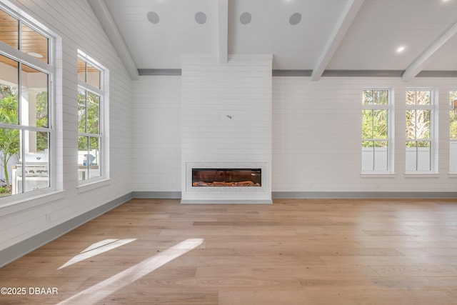 unfurnished living room with light wood-type flooring, a glass covered fireplace, beam ceiling, and baseboards