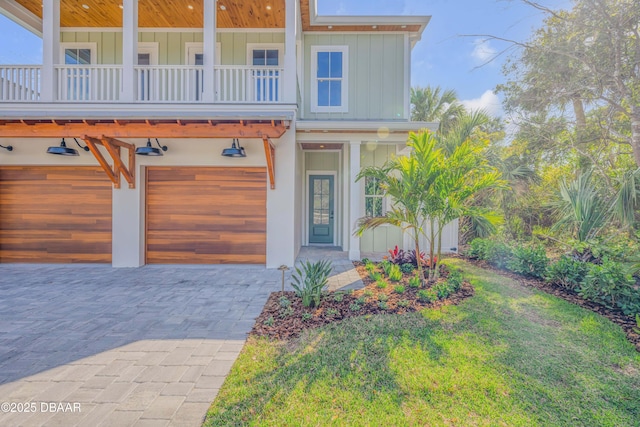 view of front facade with an attached garage, a balcony, decorative driveway, board and batten siding, and a front yard