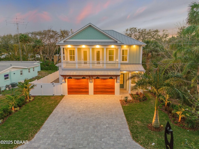 beach home with an attached garage, decorative driveway, a gate, a standing seam roof, and a front yard