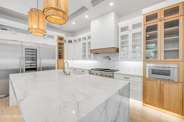 kitchen with stainless steel appliances, decorative backsplash, white cabinets, a sink, and a large island with sink