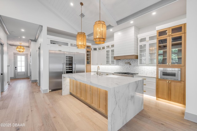 kitchen featuring a spacious island, custom range hood, light wood-style flooring, appliances with stainless steel finishes, and a sink