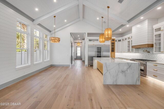 kitchen featuring premium appliances, beam ceiling, a large island, backsplash, and light wood-style floors