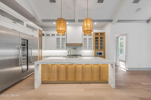 kitchen featuring stainless steel built in refrigerator, beamed ceiling, light wood-style flooring, and decorative backsplash