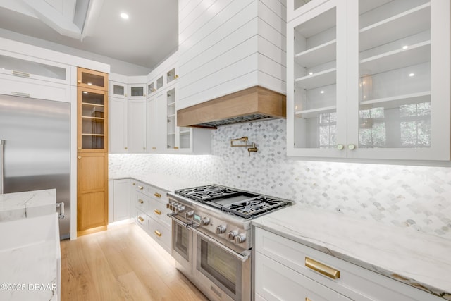 kitchen with white cabinets, light stone countertops, high end appliances, and light wood-style floors