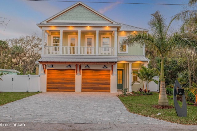 coastal home featuring decorative driveway, a gate, a standing seam roof, a balcony, and a garage