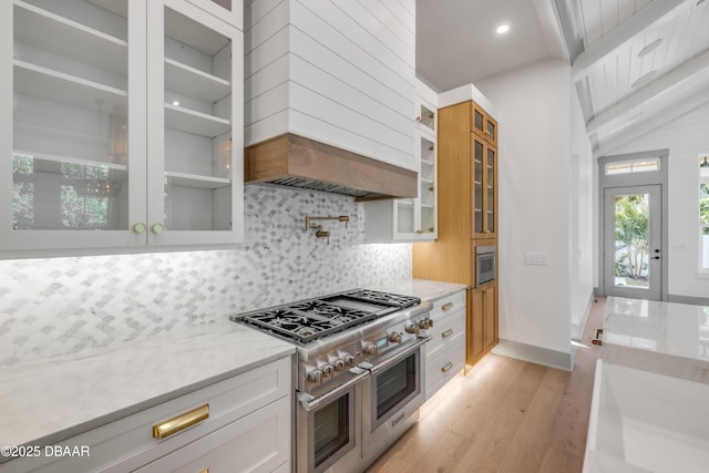 kitchen with light stone counters, light wood-style flooring, decorative backsplash, white cabinets, and double oven range