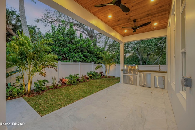 view of patio featuring ceiling fan, exterior kitchen, a fenced backyard, and a grill