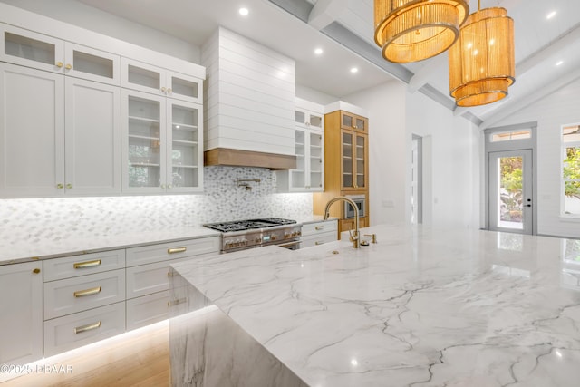 kitchen featuring vaulted ceiling with beams, light stone countertops, white cabinetry, decorative backsplash, and stainless steel range