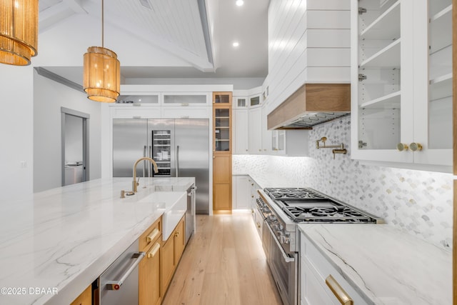 kitchen featuring premium appliances, tasteful backsplash, light wood-style floors, a sink, and premium range hood