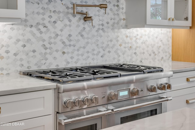 kitchen featuring light stone counters, backsplash, glass insert cabinets, white cabinetry, and double oven range