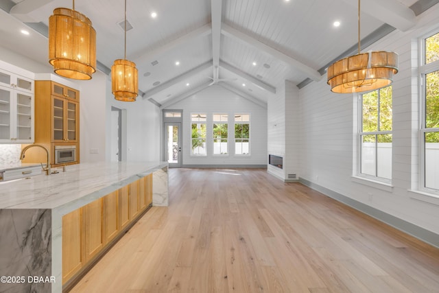 kitchen with vaulted ceiling with beams, light wood-style flooring, a sink, open floor plan, and light stone countertops