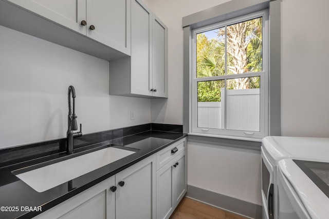 kitchen with a sink, baseboards, independent washer and dryer, dark wood-style floors, and dark countertops